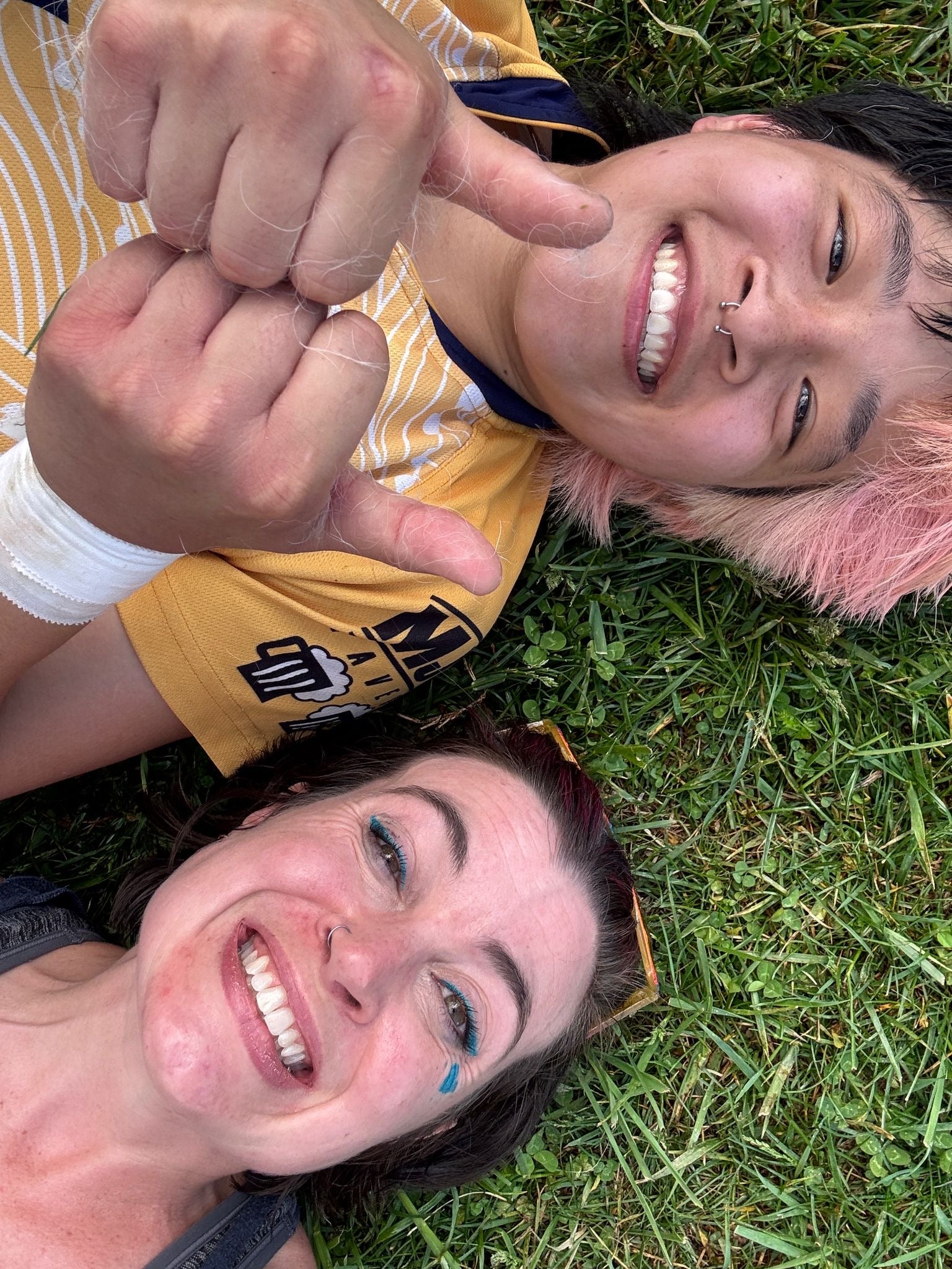 Two rugby players laying down in the grass. One is giving a double thumbs up.