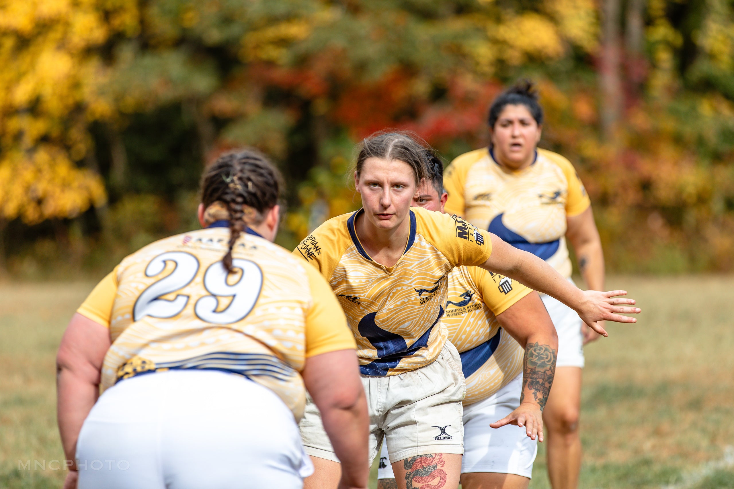 Women rugby players preparing for a lineout with fall foliage in the background.