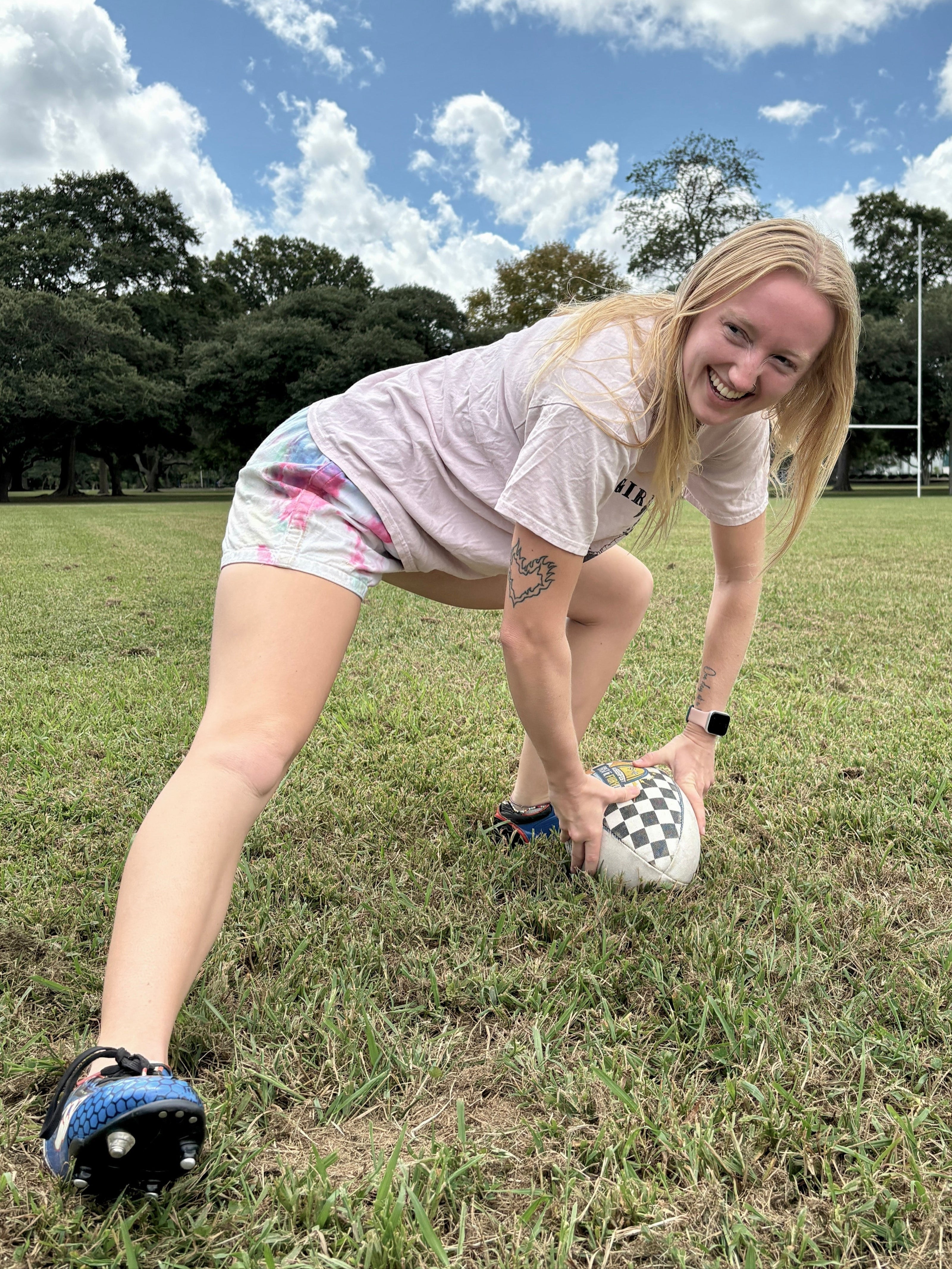 Scrum half preparing to pass a rugby ball off the ground in a grassy field with rugby posts in the background.