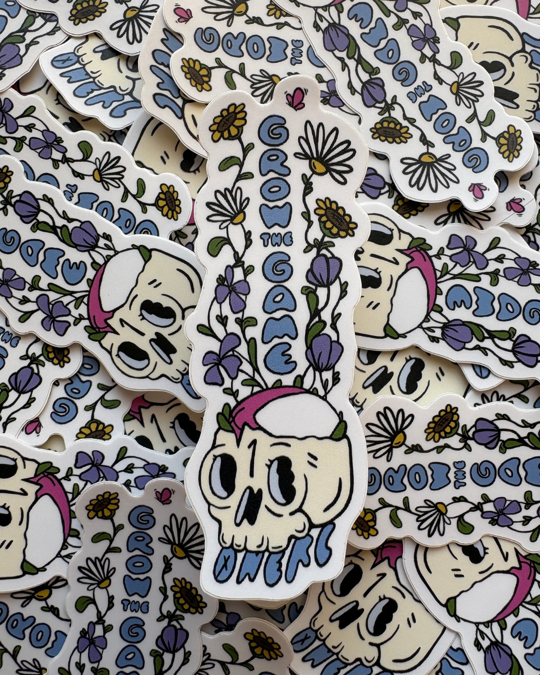 Pile of stickers of wildflowers growing out of a skull with a rugby ball resting in it.
