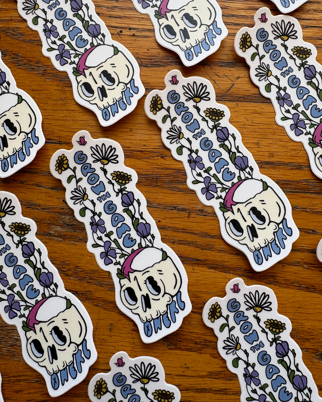 Repeating rows of stickers of wildflowers growing out of a skull with a rugby ball resting in it.