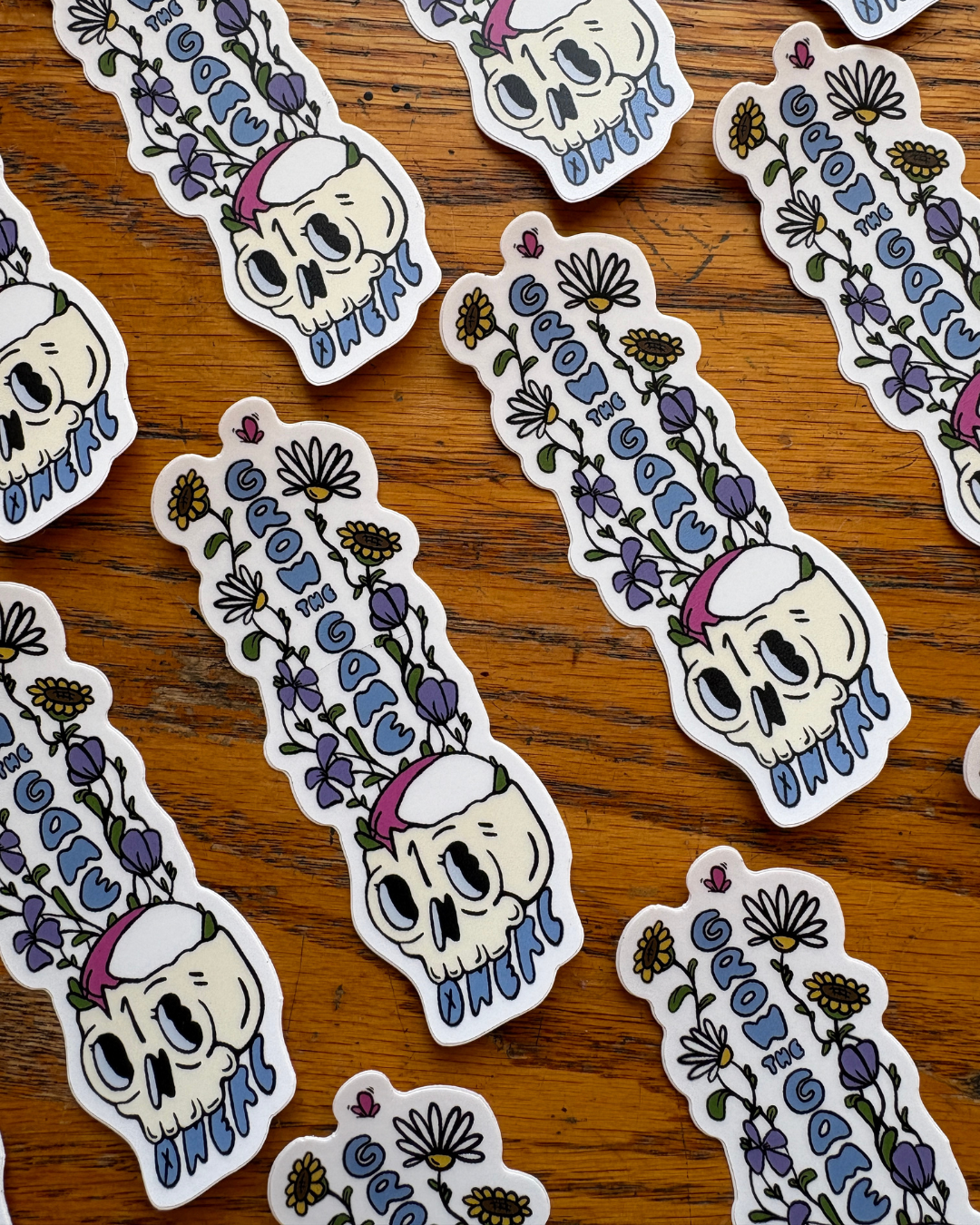 Repeating rows of stickers of wildflowers growing out of a skull with a rugby ball resting in it.