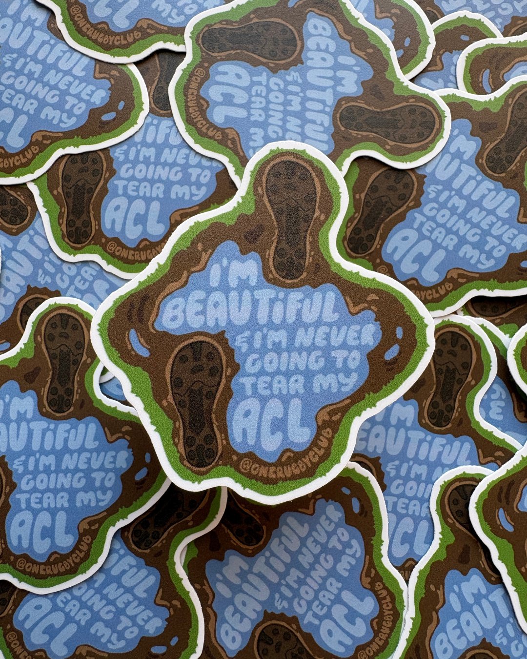 Pile of stickers of muddy cleat prints around a puddle that reads "I'm beautiful & I'm never going to tear my ACL"