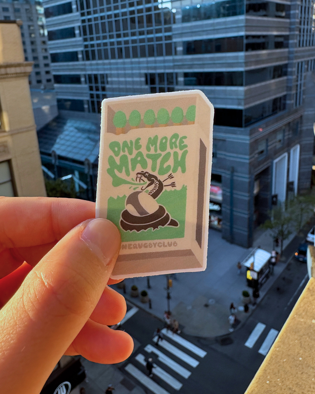 Hand holding sticker of matchbox with venomous snake and the words "One more match"