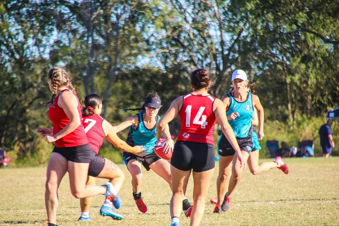 Group of women playing touch rugby with trees in the background.
