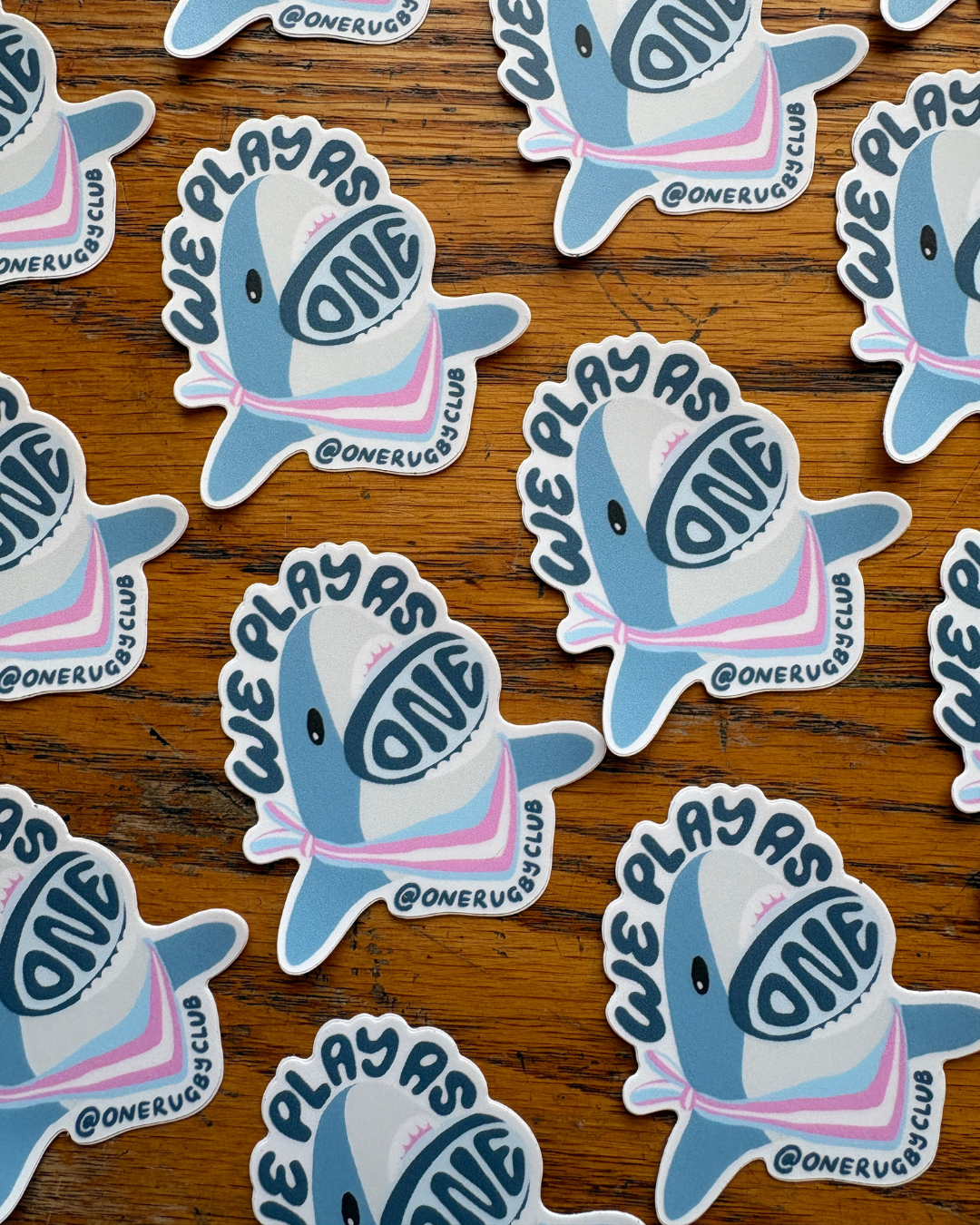 Repeating rows of trans-color, "We Play As One", rugby shark stickers.