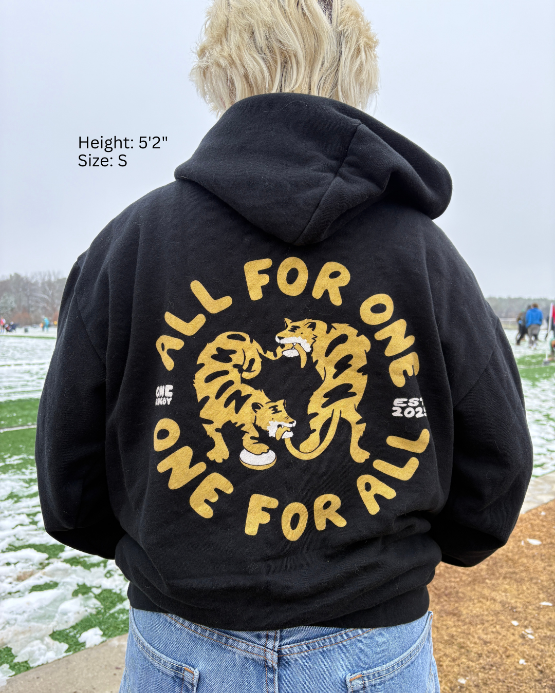 Woman wearing an "All for One, One for All" hoodie showing off the back design to the camera.