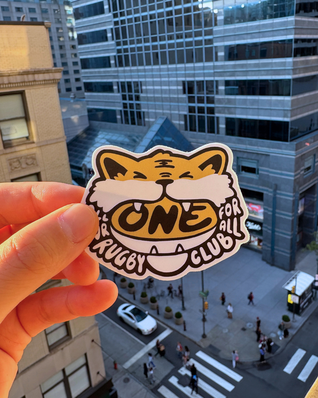 Hand holding sticker of cartoon tiger biting down on a rugby ball