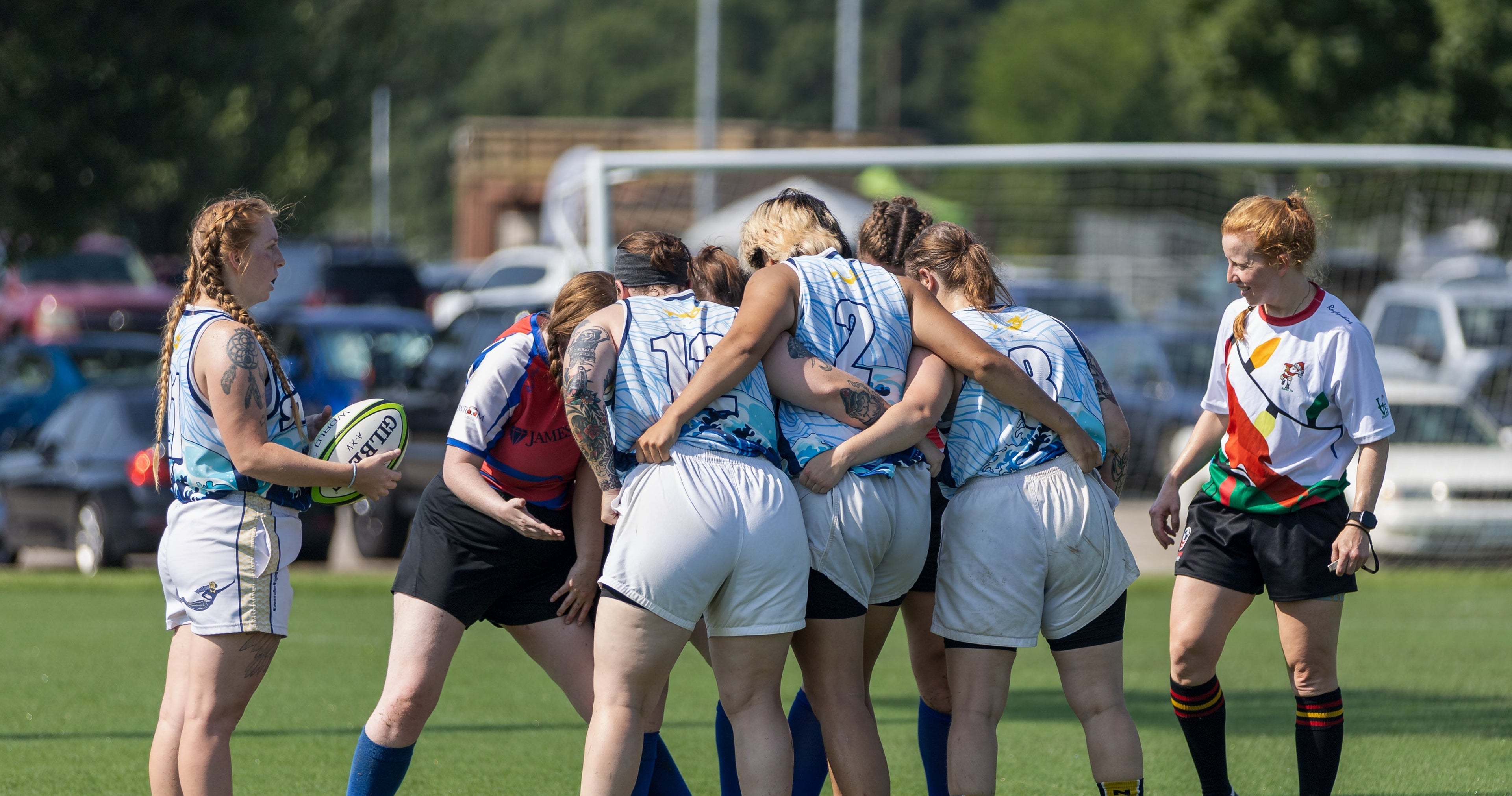 Sevens rugby players in a 3 person scrum with a scrum half holding a rugby ball on the left and a referee to the right